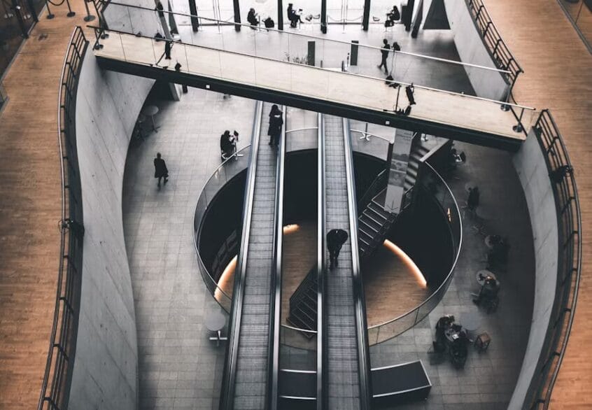 L’Avantage Fiscal du Luxembourg : Pourquoi Déménager Votre Bureau dans le Grand-Duché Peut Tout Changer 1 Vue en plongée d'un espace de bureau spacieux avec des escalators, un plafond en verre, et des personnes marchant sur un pont