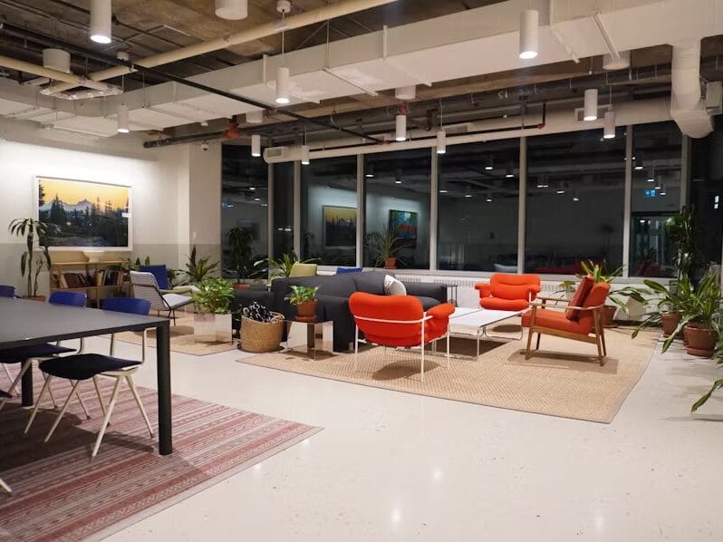 Coin détente dans un espace de coworking avec canapés, fauteuils colorés, tapis naturels, plantes d’intérieur et une ambiance chaleureuse en soirée.
