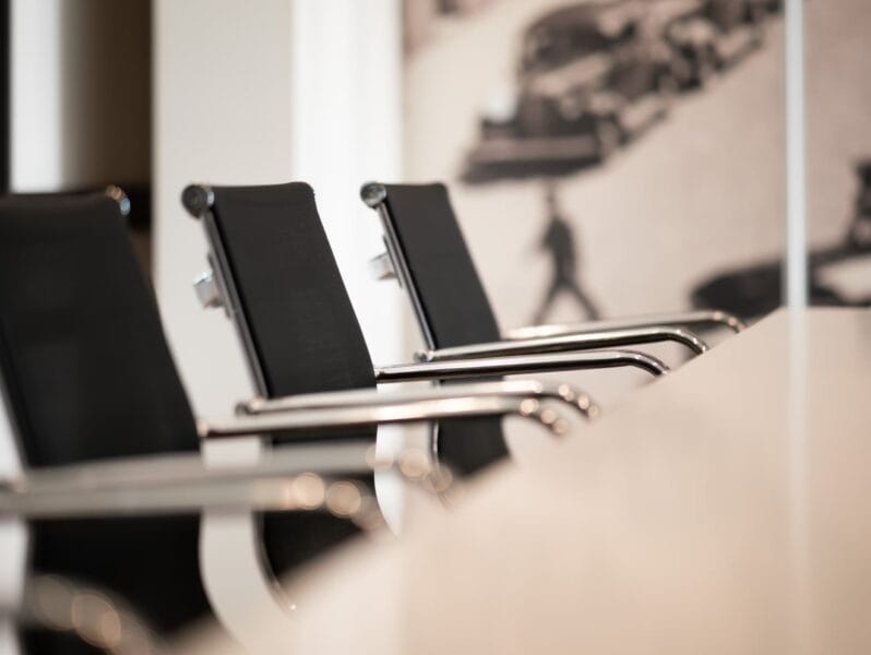 Gros plan sur des chaises de réunion noires au design élégant avec accoudoirs en métal autour d'une table blanche.