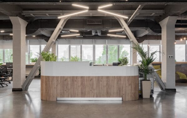 Comptoir d’accueil contemporain en bois clair dans un espace de bureau ouvert avec luminaires design et plantes vertes